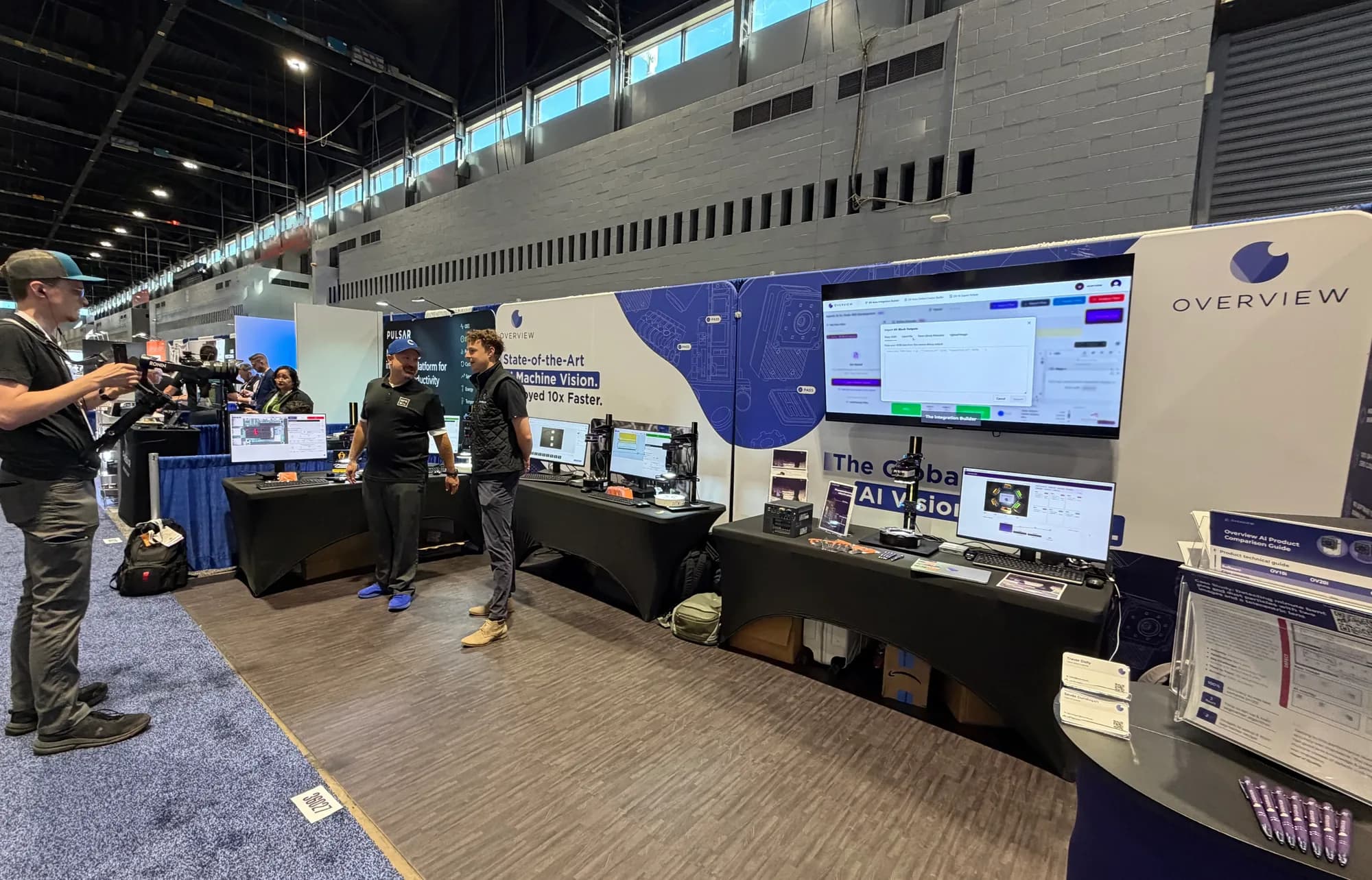 El stand de Overview AI en la feria con estaciones de inspección en vivo, pantallas mostrando el software de inspección y el equipo conversando con visitantes
